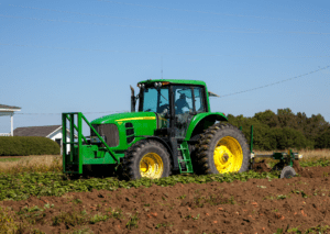 A tractor working in a field on a clear day, with a farmhouse in the background, representing farm machinery and agriculture.