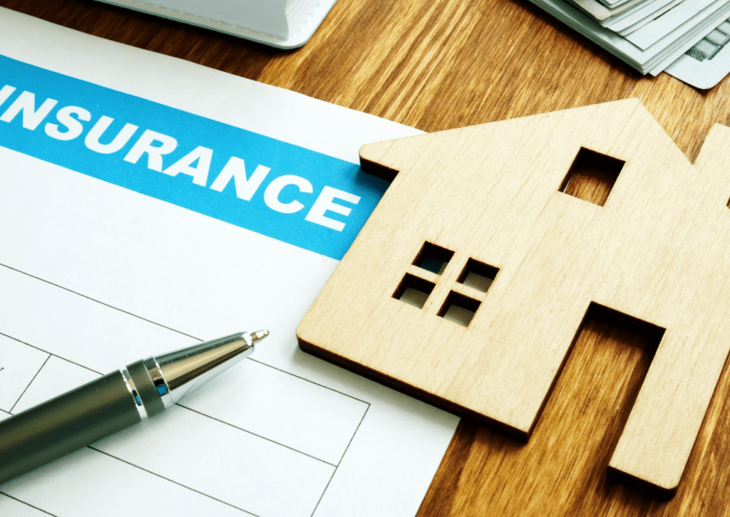 Wooden house model sits on top of a home insurance document, highlighting the importance of securing home insurance coverage.