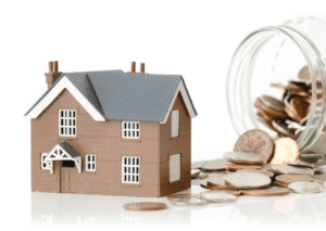 House model next to a jar of spilled coins, symbolizing savings, home investment, and financial planning for homeownership.