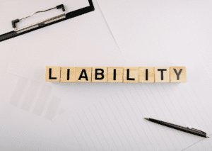 Wooden blocks spelling "LIABILITY" on a desk with scattered papers and pen, emphasizing the concept of legal responsibility.