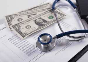 Stethoscopes and dollar bills are placed on top of medical bills, symbolizing the cost of healthcare and health insurance.