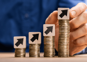 Hand stacking coins with upward arrow blocks on top, representing financial growth and increasing savings or investments.