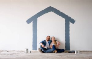 A couple sits under a painted house, symbolizing Home Insurance Greeley CO protection for new homeowners during renovations.