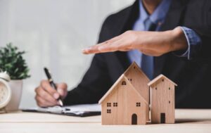 Business people hand over wooden house models and other handwriting. Depicts insurance or real estate professionals at work.