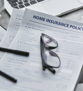 Home insurance policy document with glasses and a pen on a desk.