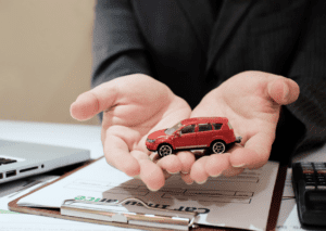 Hands holding a red toy car over documents, symbolizing auto insurance in Fort Collins and coverage protection.