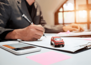 Signing an auto insurance policy with a toy car and calculator symbolizes vehicle coverage and financial planning.