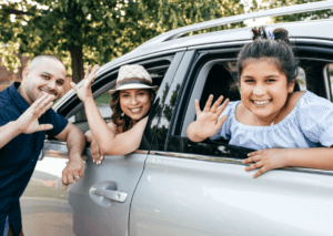 Happy family waving from their car, representing safe travels and the importance of car warranty protection.