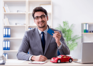 A man holding a credit card with a toy car on his desk symbolizes car and financial planning services.